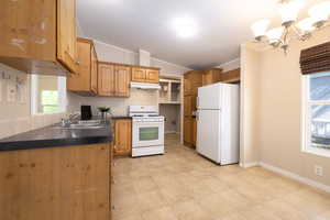 Kitchen featuring white appliances, a sink, under cabinet range hood, lofted ceiling, and dark countertops, with solid oak cabinets