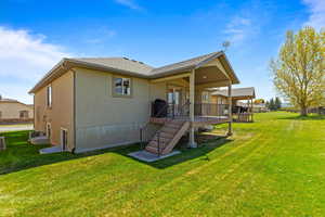Rear view of property featuring a lawn, stucco siding, a wooden deck, and central AC