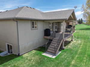 Rear view of property with roof with shingles, a lawn, and stucco siding