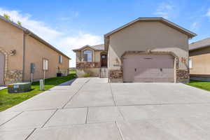 View of front of home with stucco siding, driveway, a garage, stone siding, and central AC unit