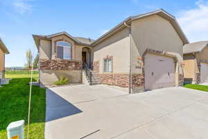 View of front of property featuring stone siding, driveway, stucco siding, and an attached garage