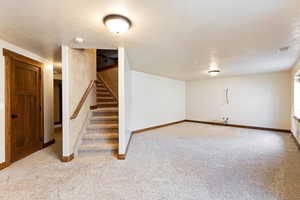 Finished below grade area featuring carpet flooring, baseboards, and stairway