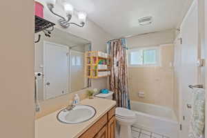 Bathroom with toilet, vanity, shower / bath combo with shower curtain, a textured ceiling, and tile patterned floors
