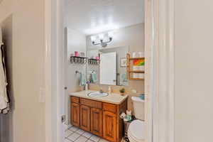 Half bath featuring toilet, a textured ceiling, tile patterned floors, and vanity