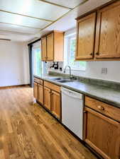 Kitchen featuring dishwasher, a sink, light wood-style flooring, and brown cabinetry