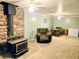 Carpeted living room with a wood stove, ceiling fan, ornamental molding, a textured ceiling, and baseboards