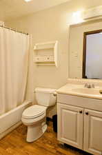 Bathroom featuring wood finished floors, toilet, vanity, shower / tub combo, and a textured ceiling
