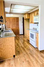 Kitchen with white appliances, a sink, and light wood-style flooring