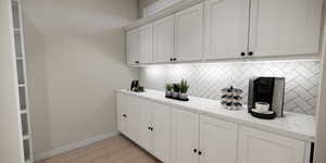 Bar featuring backsplash, white cabinetry, light wood-type flooring, and light stone countertops