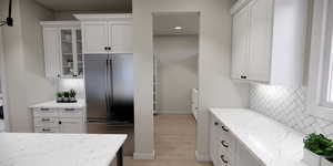 Kitchen featuring tasteful backsplash, white cabinetry, refrigerator, light stone counters, and recessed lighting