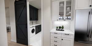 Laundry room featuring a barn door, washer / clothes dryer, light wood-type flooring, and cabinet space