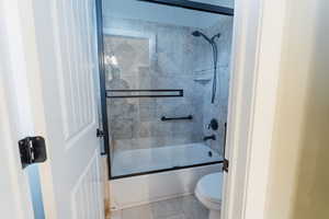 Bathroom with toilet, shower / bath combination with glass door, and tile patterned flooring