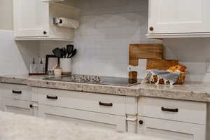 Kitchen featuring backsplash, white cabinetry, black electric stovetop, and light stone counters