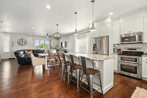 Kitchen featuring appliances with stainless steel finishes, open floor plan, decorative backsplash, light stone countertops, and a kitchen breakfast bar