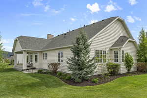 Back of house featuring a shingled roof, a patio area, a yard, and a chimney