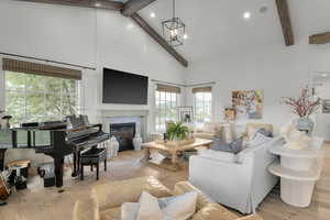 Living area featuring beamed ceiling, hardwood / wood-style flooring, high vaulted ceiling, a glass covered fireplace, and a chandelier