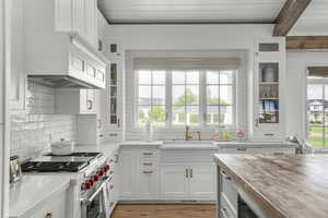 Kitchen featuring butcher block counters, high end stainless steel range, a sink, white cabinetry, and beamed ceiling