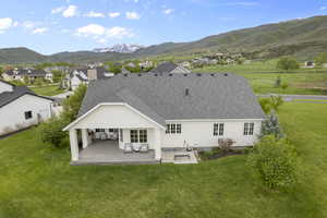 Back of property featuring a mountain view, a patio, roof with shingles, and a yard