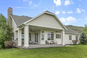 Back of house featuring ceiling fan, a lawn, a chimney, roof with shingles, and a mountain view