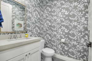 Half bathroom featuring wallpapered walls, toilet, tile patterned flooring, vanity, and baseboards