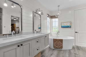 Full bath featuring a soaking tub, double vanity, wood finished floors, and wood walls