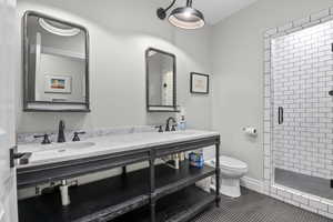 Bathroom featuring a shower stall, toilet, double vanity, and tile patterned flooring