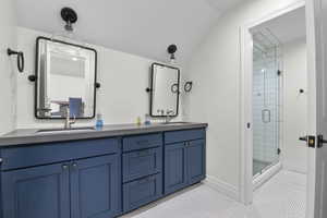 Full bath with a shower stall, double vanity, lofted ceiling, tile patterned flooring, and baseboards
