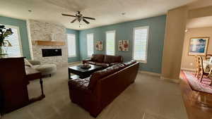 Living room with ceiling fan, a textured ceiling, baseboards, carpet flooring, and a stone fireplace