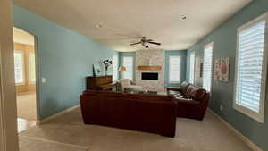 Living room with light colored carpet, a textured ceiling, ceiling fan, plenty of natural light, and a stone fireplace