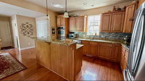 Kitchen featuring appliances with stainless steel finishes, light wood-style floors, light stone counters, and tasteful backsplash