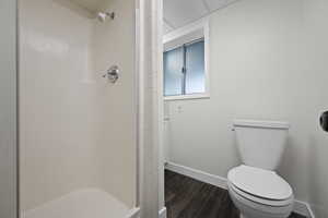 Bathroom featuring baseboards, a shower stall, wood finished floors, and toilet