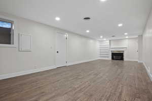 Unfurnished living room featuring wood finished floors, recessed lighting, baseboards, and built in shelves
