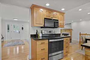 Kitchen with black microwave, stainless steel range with electric stovetop, baseboards, light wood-style flooring, and light brown cabinets