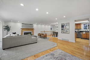 Living room featuring ornamental molding, recessed lighting, a tiled fireplace, light wood-type flooring, and baseboards
