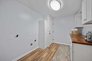 Laundry area featuring electric dryer hookup, light wood-style floors, a textured ceiling, baseboards, and cabinet space