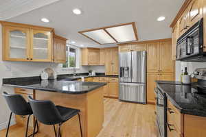 Kitchen with stainless steel appliances, a peninsula, light wood-style floors, a breakfast bar, and glass insert cabinets
