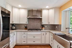 Kitchen with wall chimney exhaust hood, fridge, stainless steel gas stovetop, a sink, and backsplash