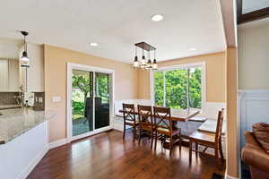 Dining room featuring dark wood finished floors, a wainscoted wall, a textured ceiling, a chandelier, and recessed lighting
