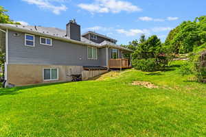 Back of house with a deck, a chimney, and a yard