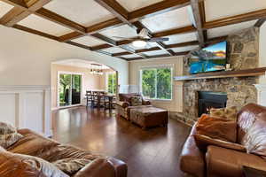 Living area with coffered ceiling, ceiling fan, a stone fireplace, arched walkways, and dark wood-type flooring