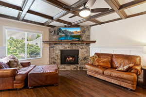 Living room with coffered ceiling, a stone fireplace, hardwood / wood-style floors, a ceiling fan, and beamed ceiling
