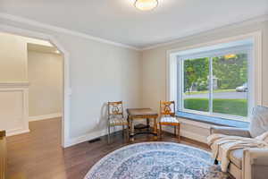 Sitting room featuring dark wood-type flooring, ornamental molding, arched walkways, and baseboards