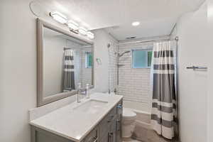 Bathroom with toilet, vanity, a textured ceiling, shower / tub combo, and recessed lighting