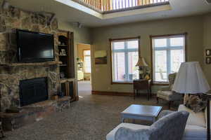 Carpeted living room featuring a stone fireplace and baseboards