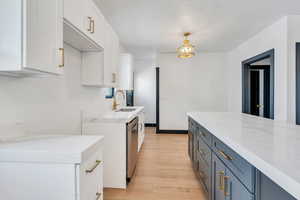 Kitchen with a sink, light wood-style flooring, white cabinets, and light stone countertops