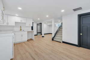 Kitchen with white cabinets, a sink, light wood-style floors, and recessed lighting