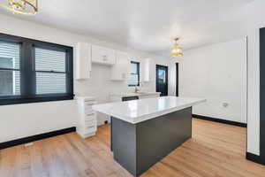 Kitchen with white cabinetry, a sink, a chandelier, baseboards, and light countertops