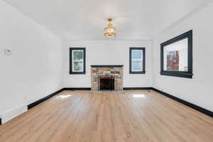 Living room with healthy amount of natural light, a stone fireplace, wood-type flooring, and baseboards