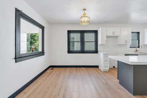 Kitchen featuring white cabinetry, light countertops, baseboards, a chandelier, and light wood-type flooring