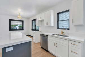 Kitchen featuring a sink, dishwasher, light wood-type flooring, white cabinetry, and light stone countertops